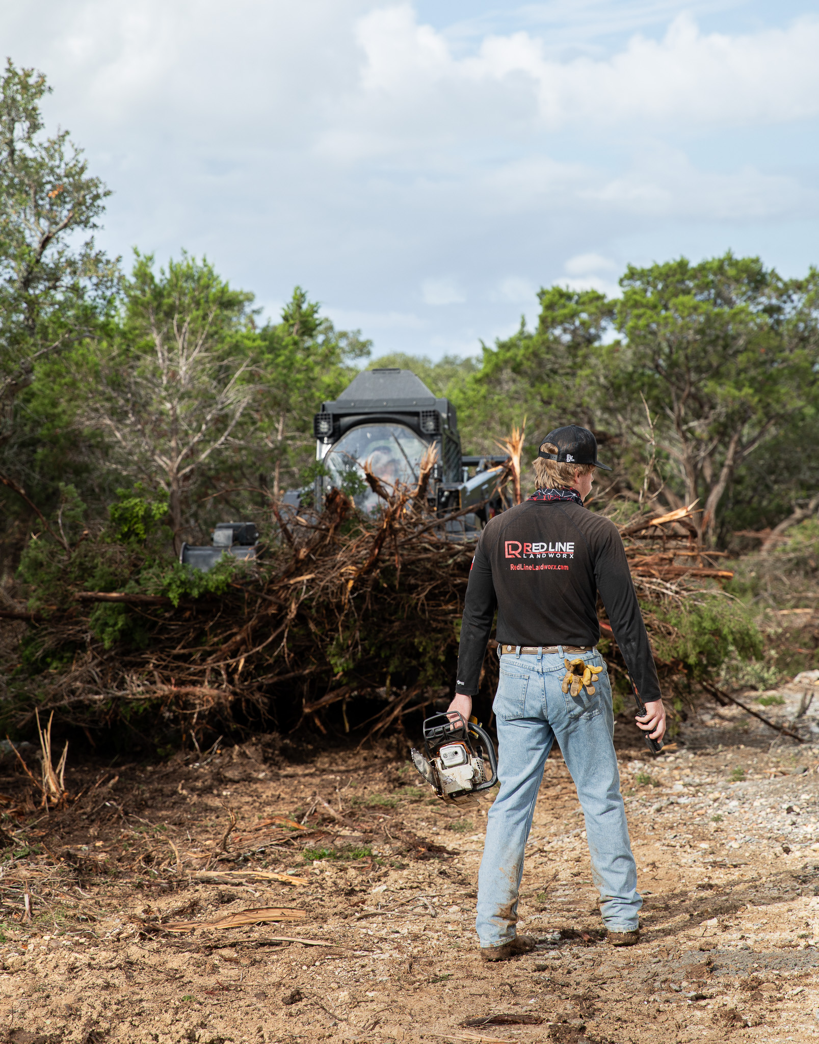 Worker carrying chainsaw past skid steer